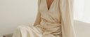 Woman sitting while wearing a beige flowy dress.