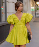 Woman wearing the neon green Gretta mini dress from AJE. in a busy city street.