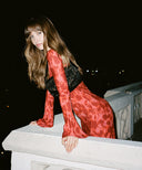 Woman with long brown hair wearing the Gia maxi dress by Realisation Par at an event, leaning over a balcony.