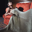 Woman wearing the gold shimmer maxi dress by L'Idée lying on a sofa with the folded texture of the fabric on display.