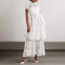 Front view of a white tiered lace maxi dress by self-portrait. The dress features a sheer lace high neck with short sleeves with an opaque fitted bust. The bottom of the dress is divided into 3 tiers of lace overlapping each other.